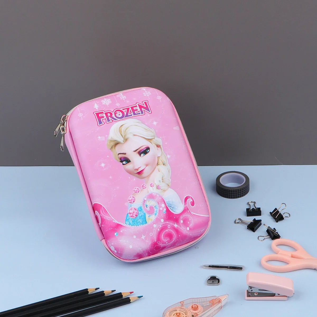 Three Frozen theme pencil cases with character illustrations, displayed alongside stationery items such as pencils and a makeup brush.