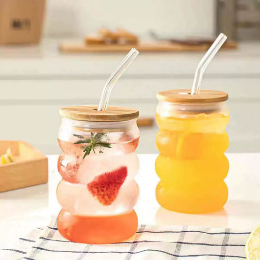 Two glass jars with wooden lids and straws, one containing a fruit-infused drink and the other with a yellow liquid.