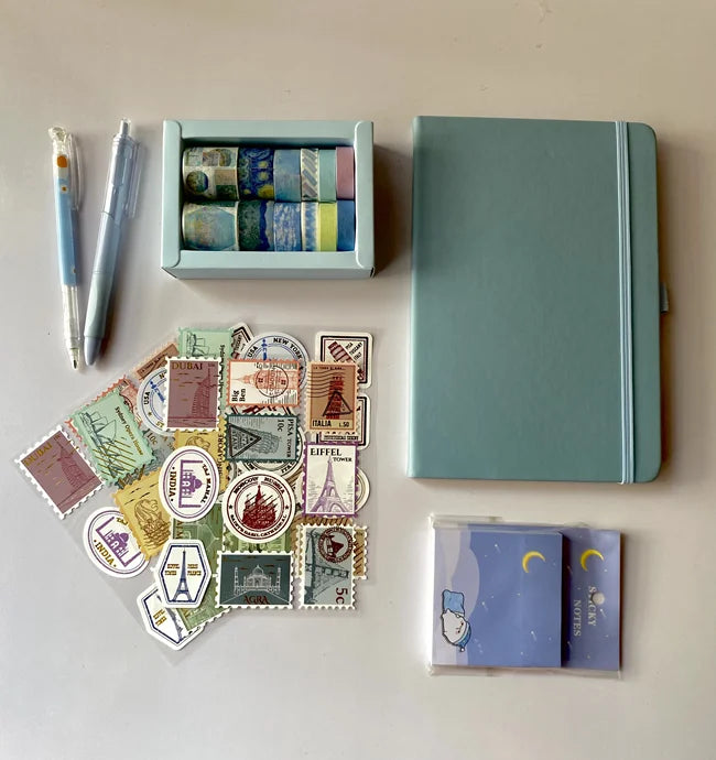 Collection of stationery items including a notebook, pens, and postcard designs on a light background