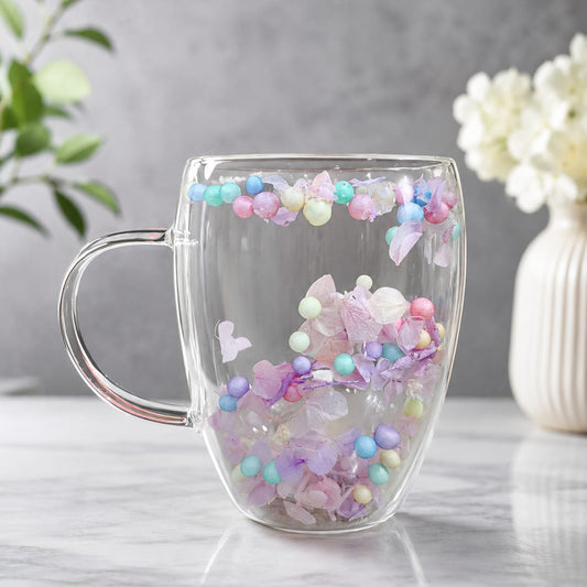 Clear mug with colorful beads and heart decorations on a light gray surface.