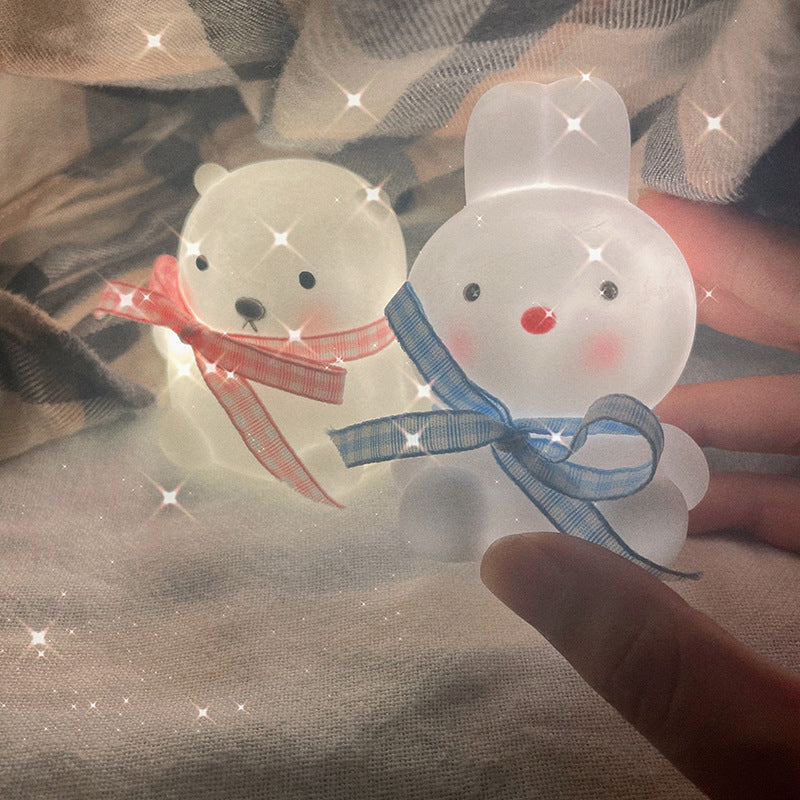 Two transparent rabbit-shaped objects with ribbons held against a textured fabric background.