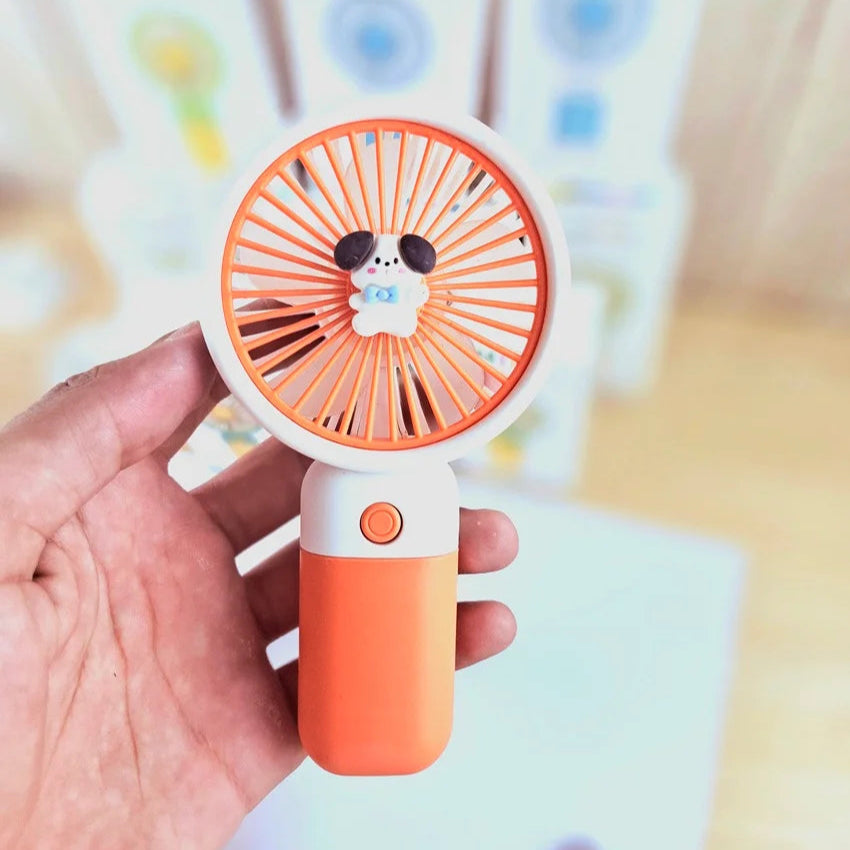 Hand holding a small orange fan with a dog design on a blurred background