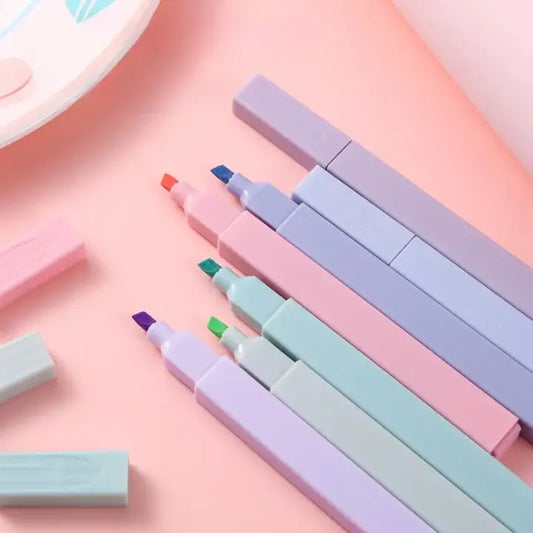 Set of pastel-colored markers and erasers on a pink background