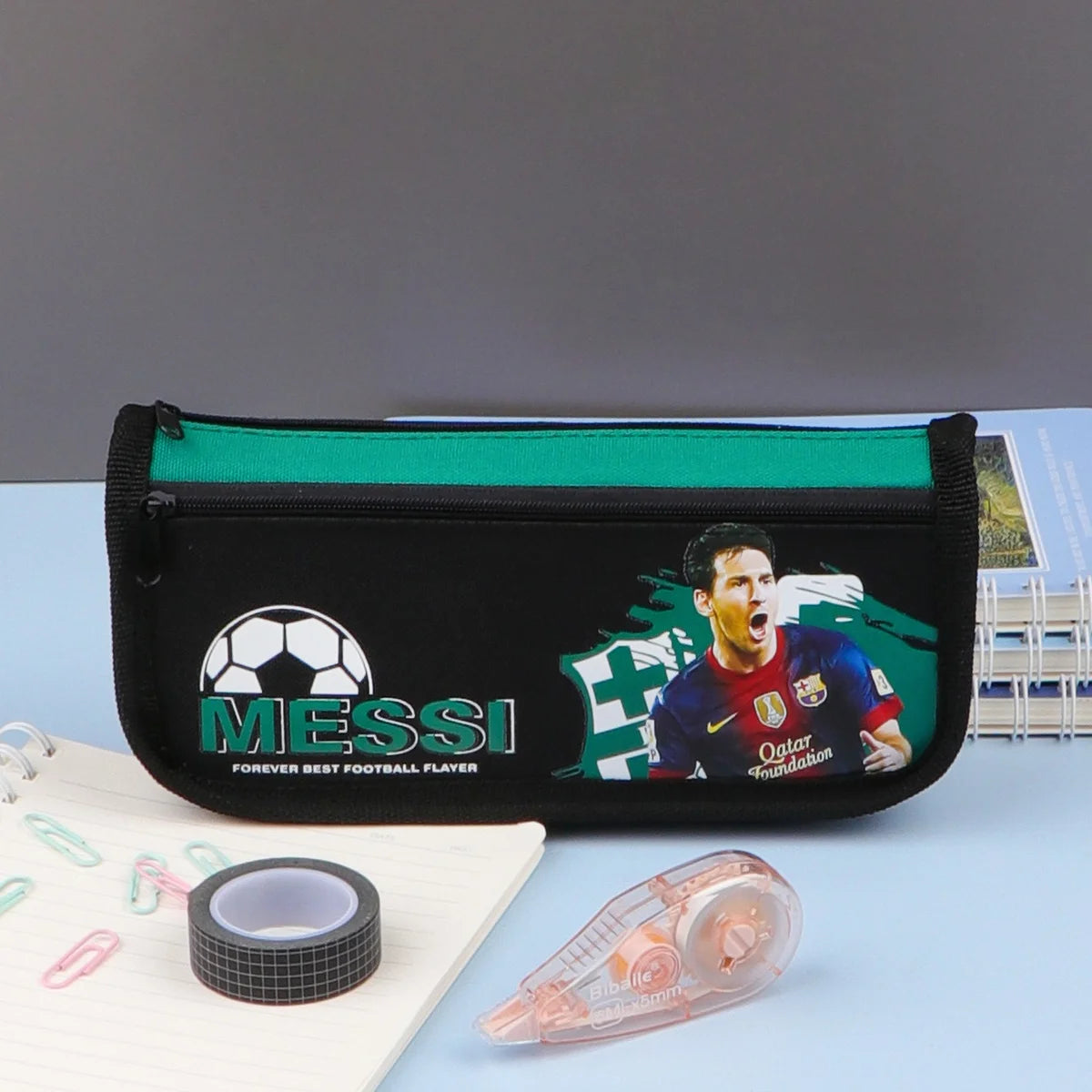 A pencil case with a zipper closure, featuring a soccer player on a blue background, and additional compartments. The pencil case is displayed in packaging labeled 'SCHOOL'.