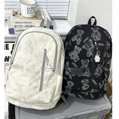 Two backpacks, one white and one black with bear patterns, on a surface.