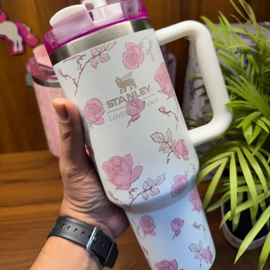 Stanley mug with floral design held by a hand, with a plant in the background