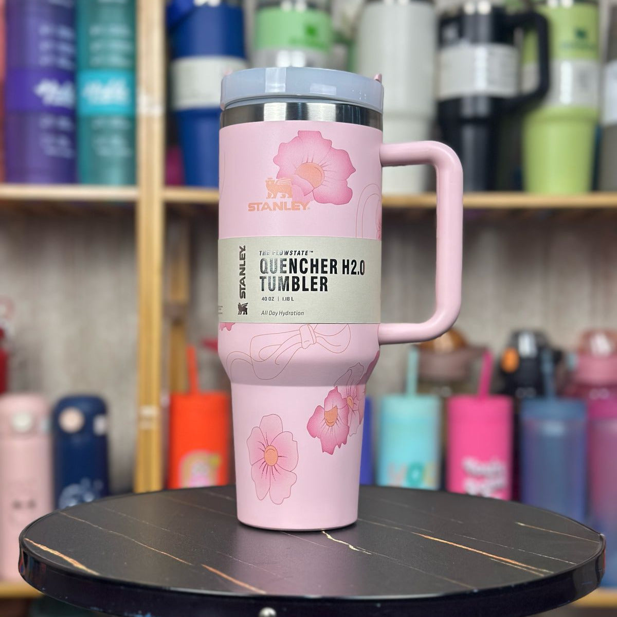Pink tumbler with floral design on a round black table against a background of various colorful tumblers.