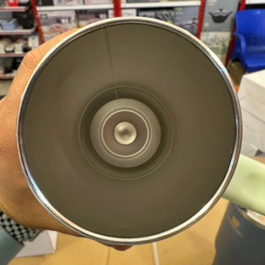 Close-up of a green mug with a metallic interior held by a hand in a store setting.