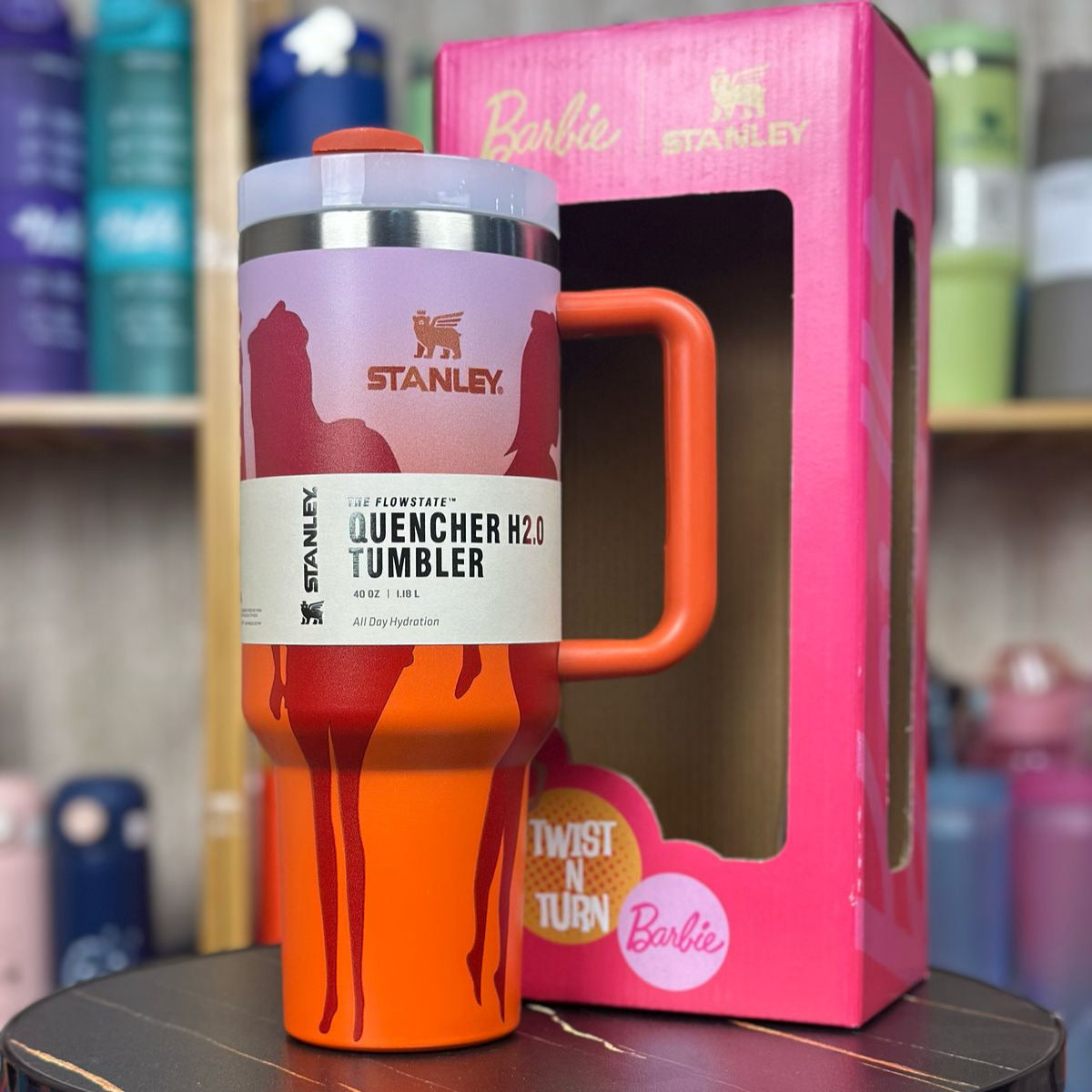 Orange Stanley tumbler with pink packaging featuring Barbie on a black surface.