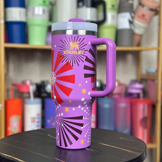 Purple Stanley tumbler on a table with shelves of other tumblers in the background