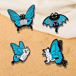 A set of four enamel pins designed as cats with butterfly wings, in blue, black, white, and yellow colors.