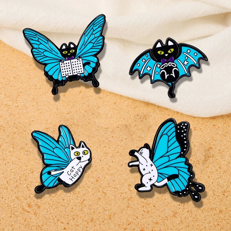 A set of four enamel pins designed as cats with butterfly wings, in blue, black, white, and yellow colors.