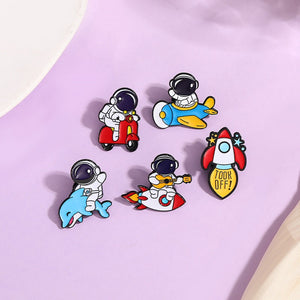 A set of colorful enamel pins featuring astronaut characters in various playful scenarios, such as riding a scooter and sitting in a rocket.