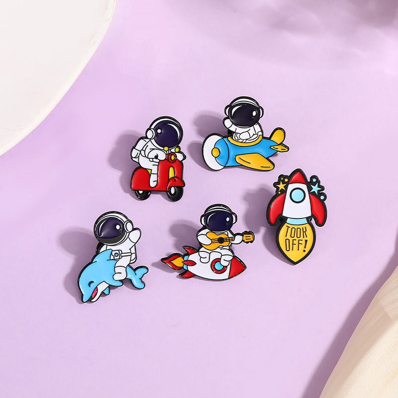 A set of colorful enamel pins featuring astronaut characters in various playful scenarios, such as riding a scooter and sitting in a rocket.