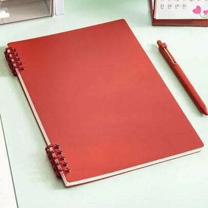 Red notebook with a pen on a light green surface