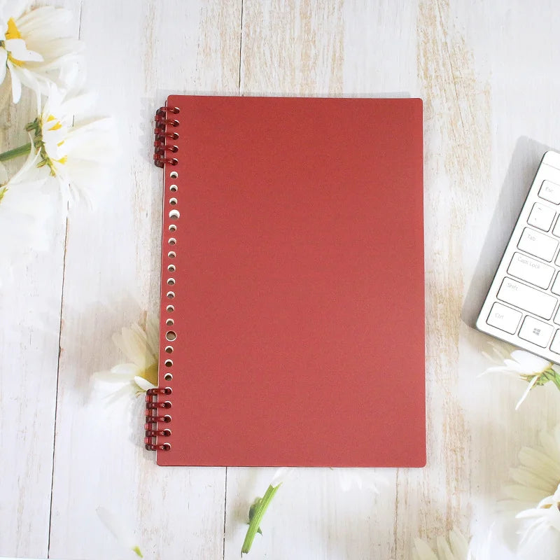 Red notebook on a light wooden surface with white flowers and a keyboard.