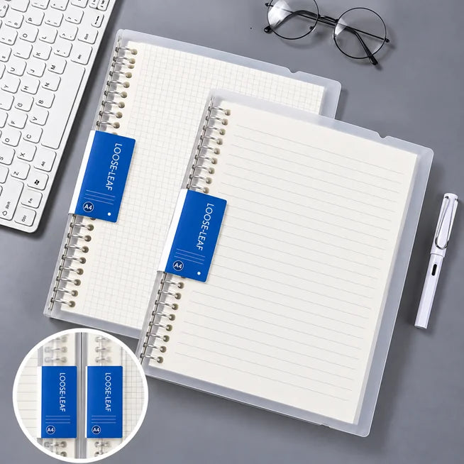 Two loose-leaf notebook inserts in clear plastic sleeves with blue tabs labeled 'LOOSE LEAF' are arranged on a gray desk beside a keyboard, glasses, and a pen. A circular inset at the bottom left shows a close-up of the blue tabs.