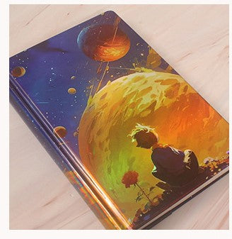 Notebook with space-themed design featuring a planet and astronaut on a wooden surface
