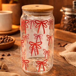 Clear glass jar with red bow pattern on a wooden surface with coffee beans and a cup.