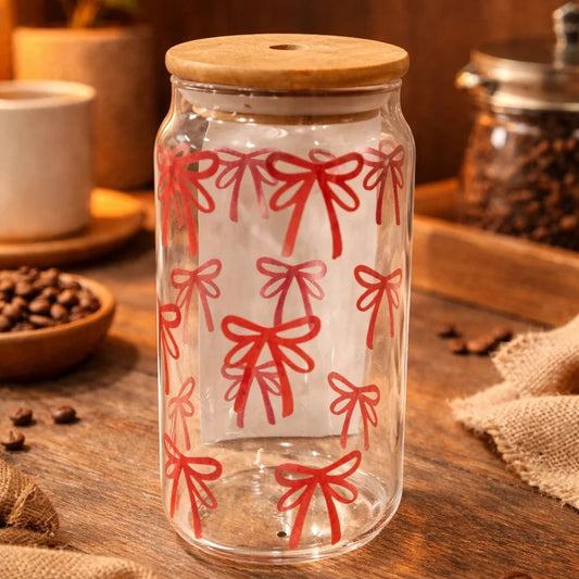 Clear glass jar with red bow pattern on a wooden surface with coffee beans and a cup.