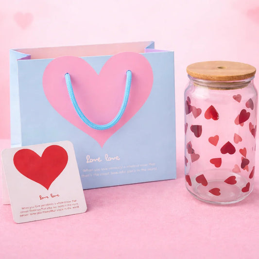 Candle jar with heart pattern, gift bag, and card on a pink background