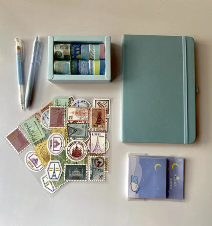 Collection of stationery items including a notebook, pens, and postcard designs on a light background