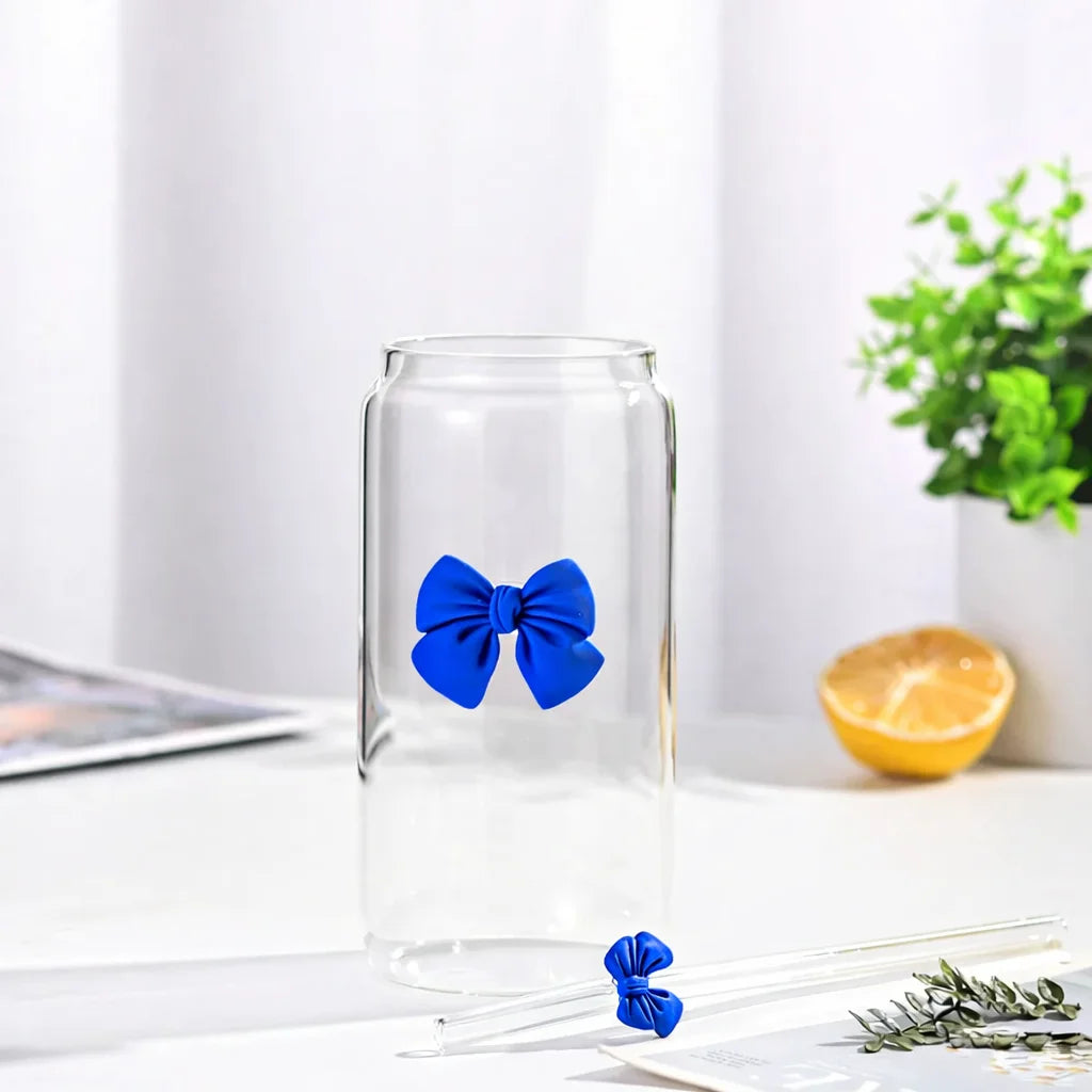 Clear glass jar with a blue bow on a white surface with a plant in the background