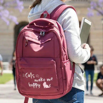 Person wearing a red backpack with 'Cats make me happy' text, holding a tablet, outdoors.