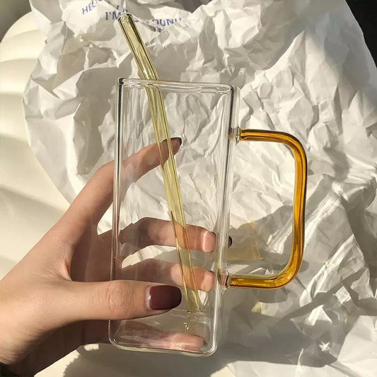 Clear glass mug with amber handle and straw held by a hand on crumpled paper background