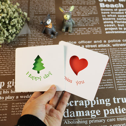 Two small greeting cards with a tree and heart design held by a hand on a newspaper background.