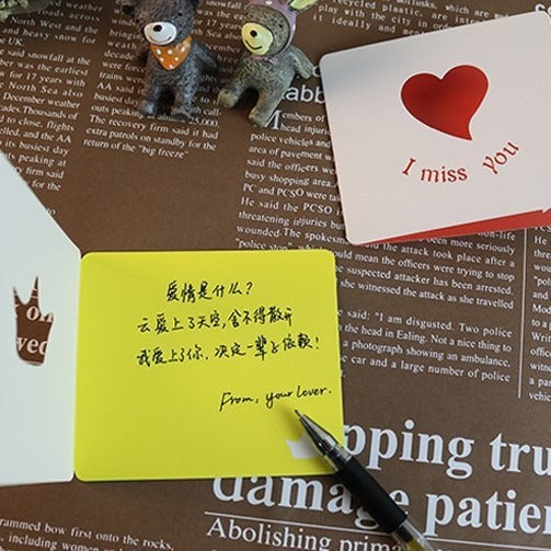 Notebook with handwritten text, small figurines, and a card on a newspaper background