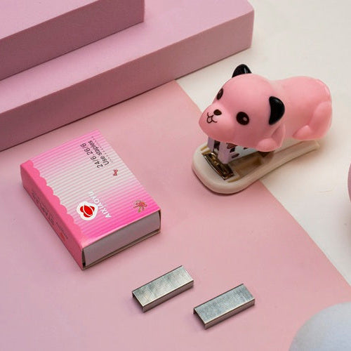 Pink desk accessory set with a small animal-shaped stapler on a pink surface.