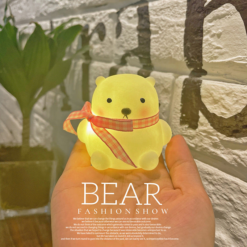 Yellow bear-shaped light with a red ribbon held in front of a stone wall.