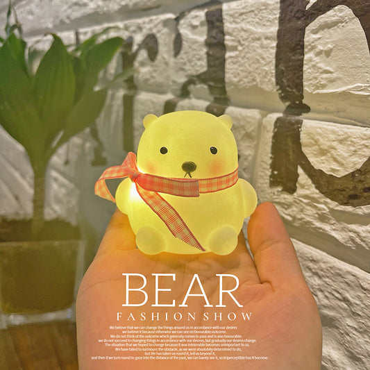 Yellow bear-shaped light with a red ribbon held in front of a stone wall.