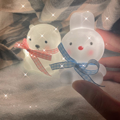 Two transparent rabbit-shaped objects with ribbons held against a textured fabric background.