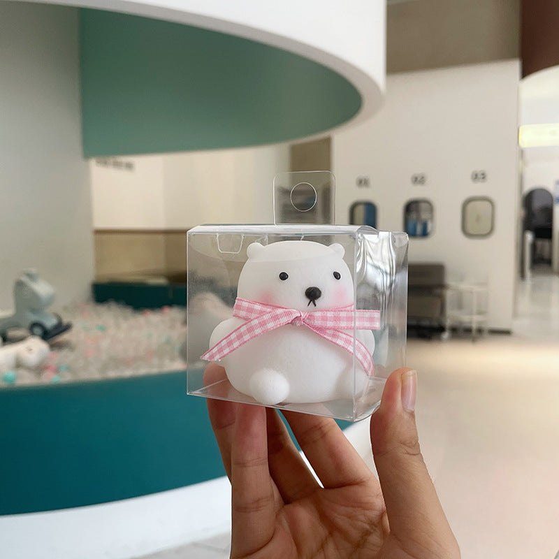 Clear plastic packaging with a white bear toy wearing a pink bow, held in front of a blurred indoor background.