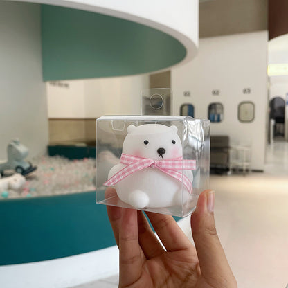 Clear plastic packaging with a white bear toy wearing a pink bow, held in front of a blurred indoor background.