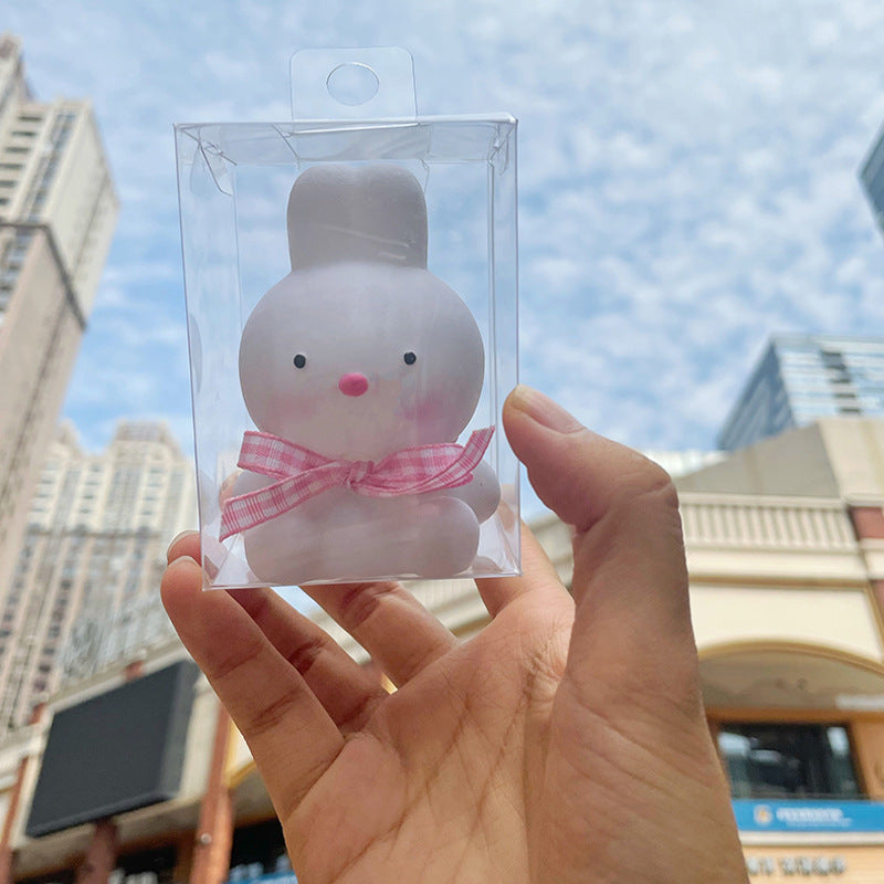 Small plush toy with a pink bow in clear packaging held against a cityscape background