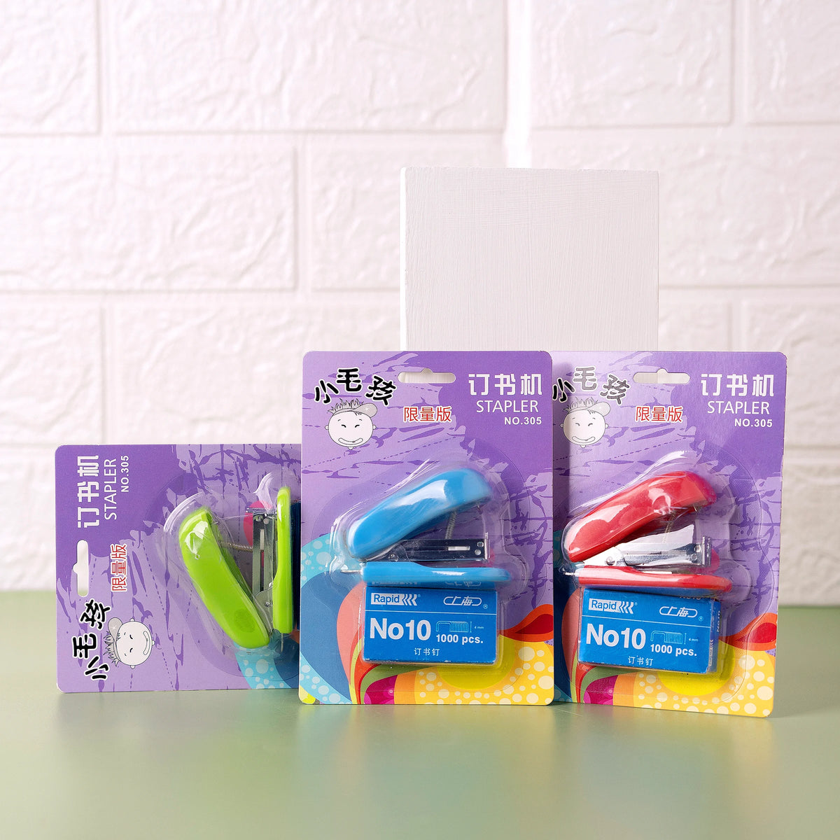 Three mini staplers with pins packaged in card boxes, displayed against a white background. Each stapler is in a different color: green, blue, and red.