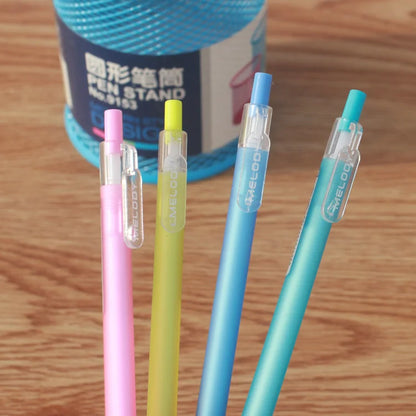 Four colorful pens with clear caps on a wooden surface, with a pen stand in the background.