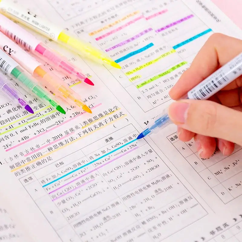 Colorful highlighters on a textbook with a hand holding a blue highlighter.