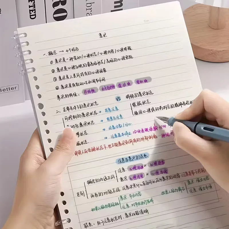 Person writing in a notebook with colorful text on a desk