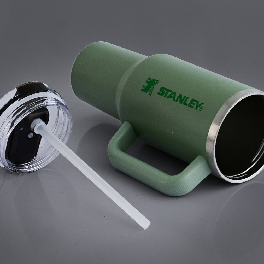 Green Stanley tumbler with a straw on a gray background