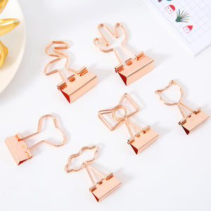 Rose gold paper clips with various shapes on a white surface