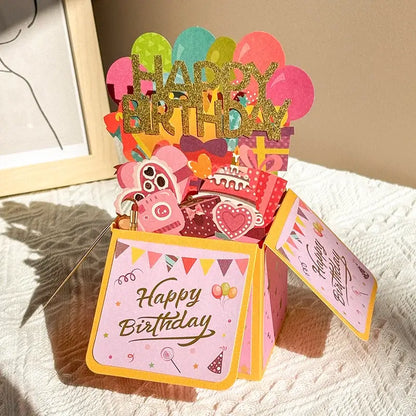Colorful birthday pop-up card with balloons and a cake on a textured surface.