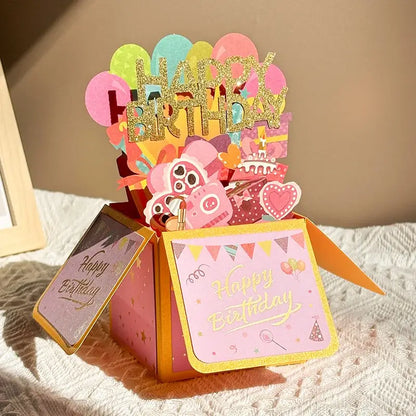 Pop-up birthday card with colorful balloons and 'Happy Birthday' text on a textured surface.