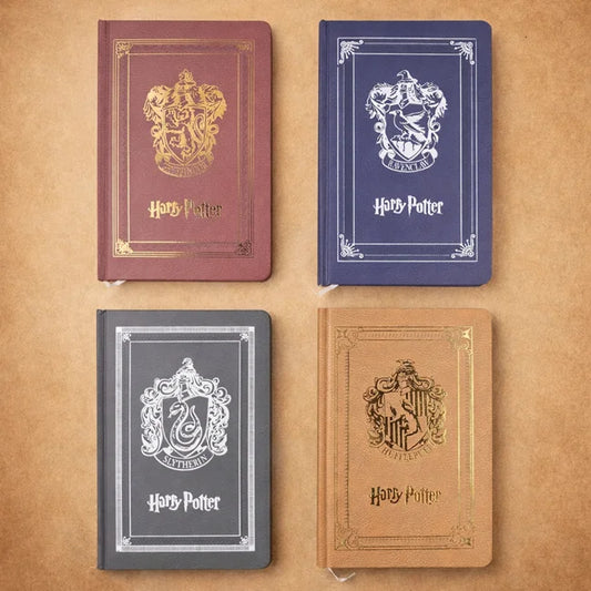 Four Harry Potter-themed notebooks with different house crests on a brown background
