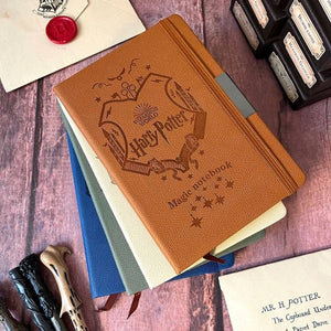 Stack of Harry Potter-themed notebooks on a wooden surface with wands and letters.