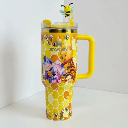A yellow Winnie the Pooh-themed travel tumbler with a honeycomb pattern, featuring characters like Pooh, Tigger, and Eeyore, a yellow handle, and a lid topped with a bee figure.