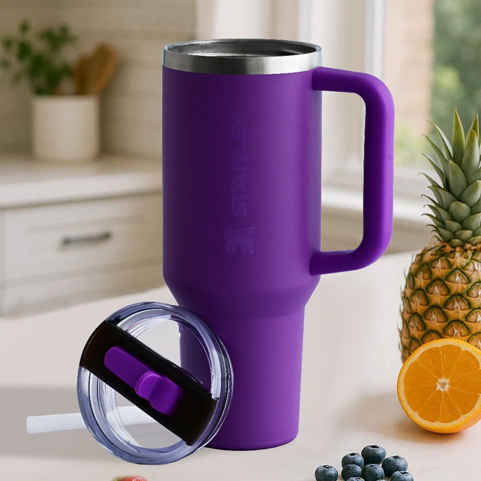 Purple travel mug with handle on a kitchen counter with fruits and a plant in the background
